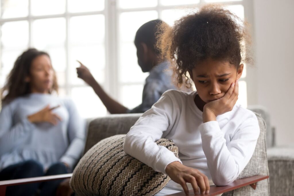 A sad child sits in the foreground while parents argue in the background, symbolizing the emotional impact of divorce on families.