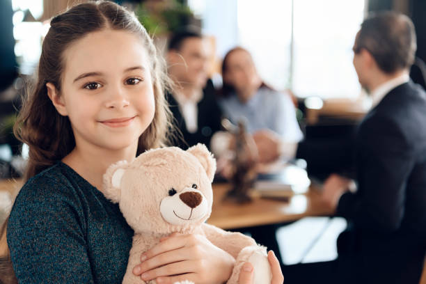 A young girl stands with a teddy bear and smiling at camera. Beautiful girl with parents stands in the office of a legal document assistant filing child custody document.